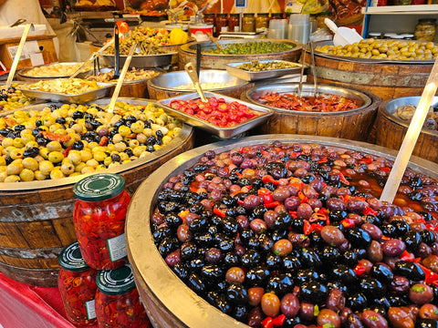 A market stall displays various olives and other foods.