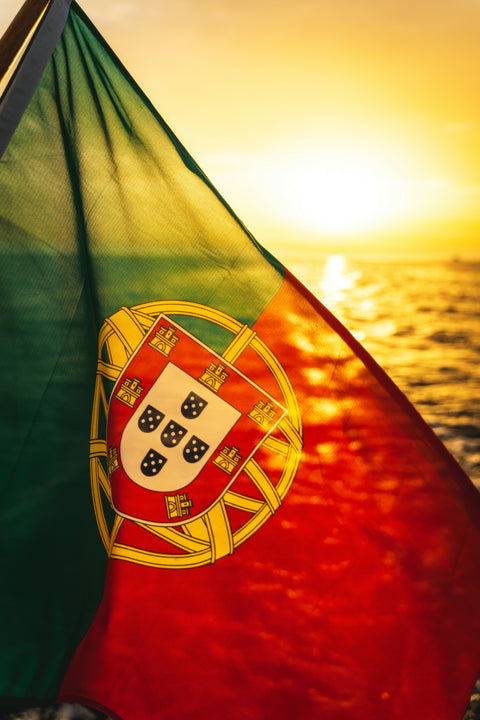 Portuguese flag waving against a sunset ocean backdrop